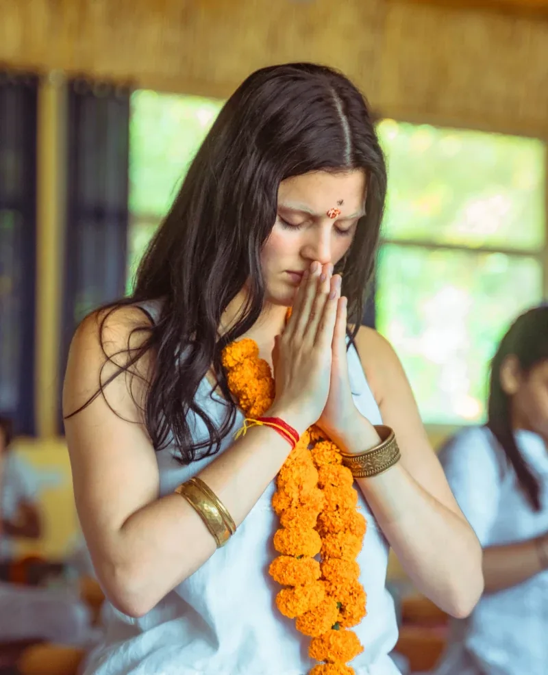 Yoga student in Namaste wearing a marigold garland at a welcome ceremony, World Peace Yoga School Rishikesh