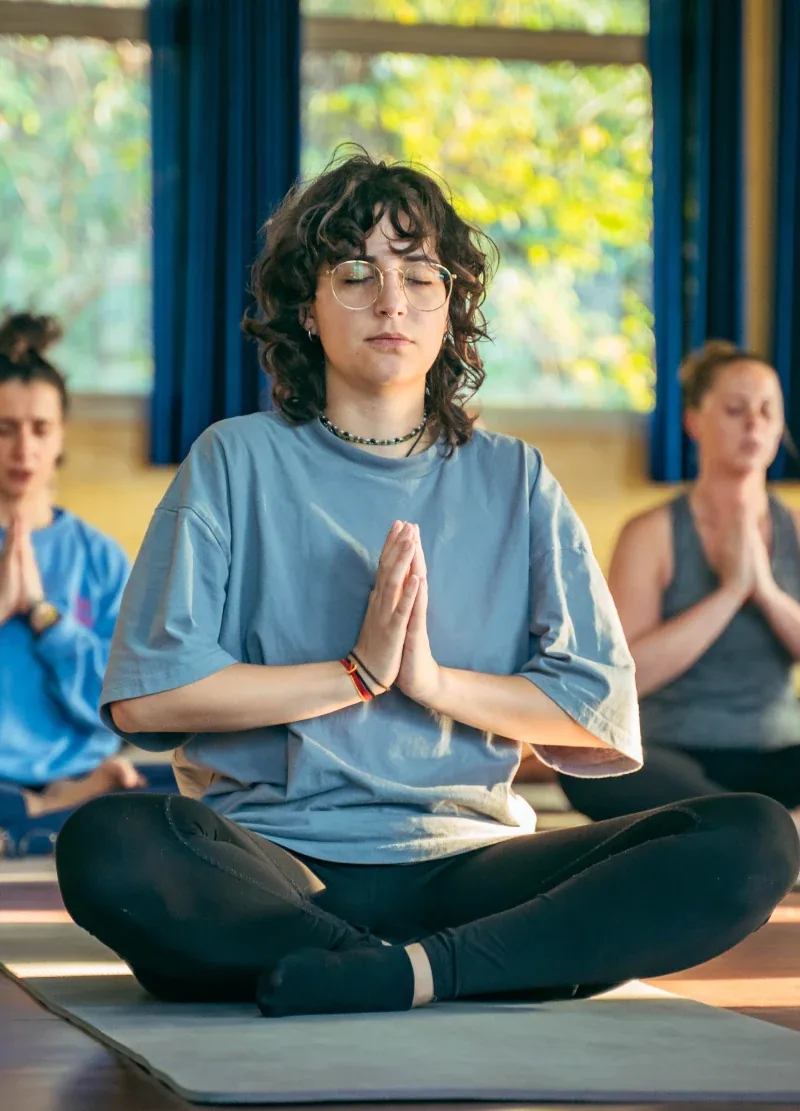Students meditating in easy pose with hands at the heart in the yoga hall in Rishikesh