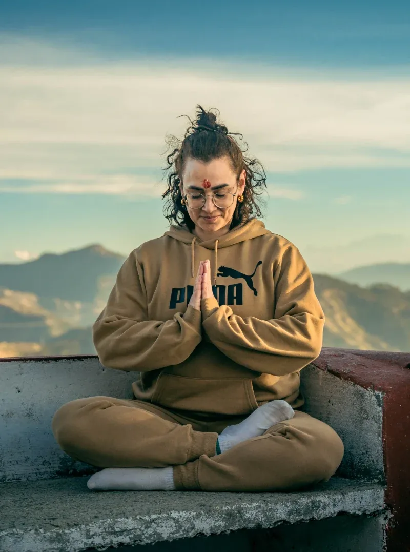 Yoga student meditating cross-legged on a rooftop overlooking the Himalayan foothills in Rishikesh