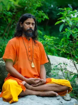 Yogi Vishnu Panigrahi meditating in lotus pose on a rock surrounded by nature