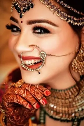 Smiling bride in traditional Indian bridal makeup with a nose ring, gold jewellery and henna-decorated hands