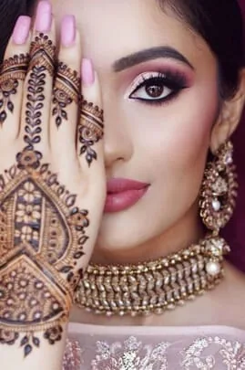Woman showing intricate henna mehndi designs on her hand, wearing bridal eye makeup and a gold choker