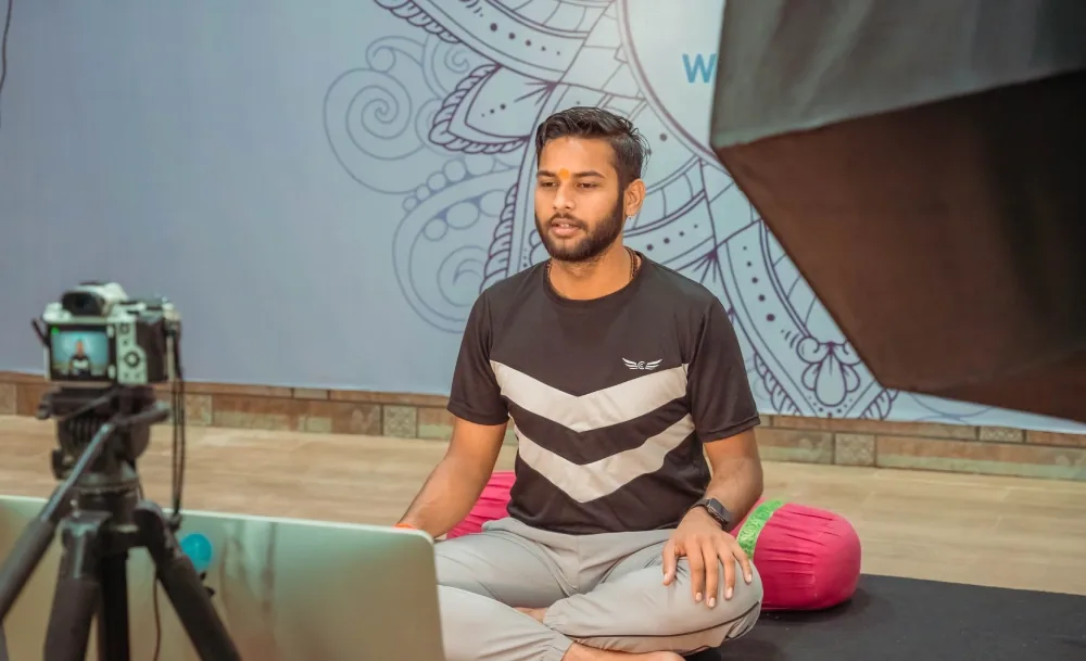 Instructor recording an online yoga teacher training class with a camera and laptop
