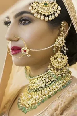 Woman in profile wearing traditional gold bridal jewellery with a nose ring, maang tikka and layered necklaces