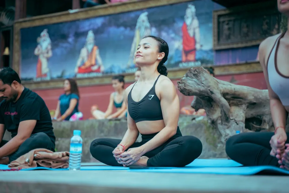 Student meditating at an open-air yoga class with Hindu sage murals behind in Rishikesh