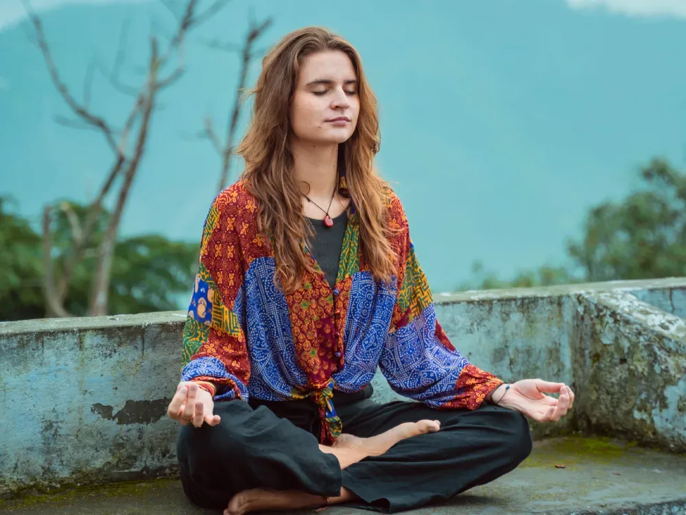 Yoga student meditating on a terrace with misty Himalayan mountains behind in Rishikesh