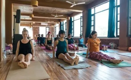 Students seated in staff pose on mats in the wooden-floored hall