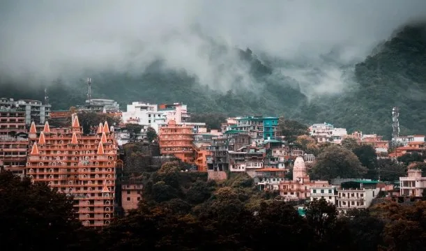 Temples and buildings of Rishikesh beneath clouded green hills