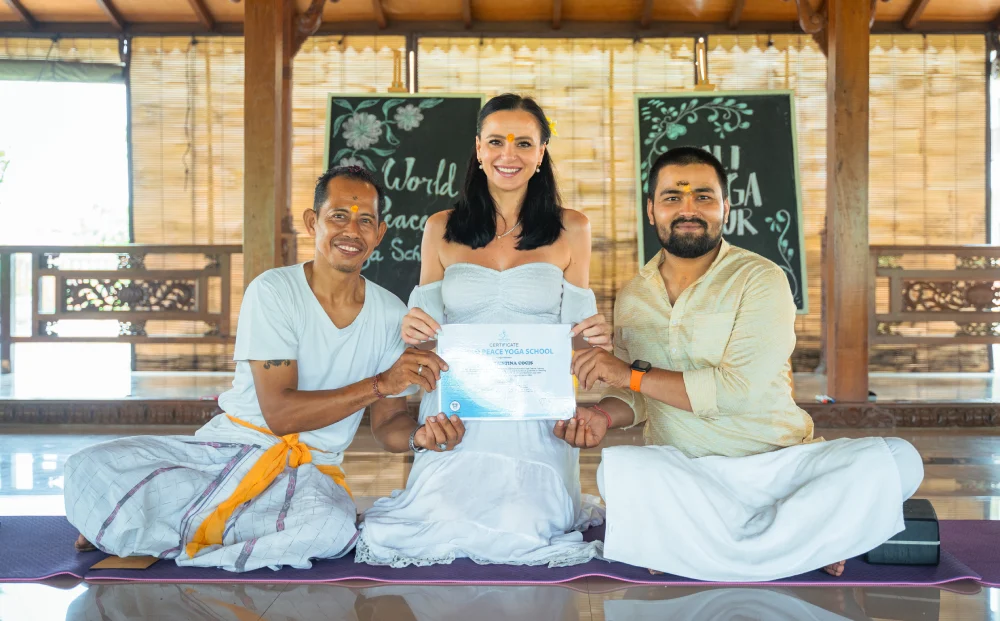 A graduate holding her certificate with two teachers in the Bali shala
