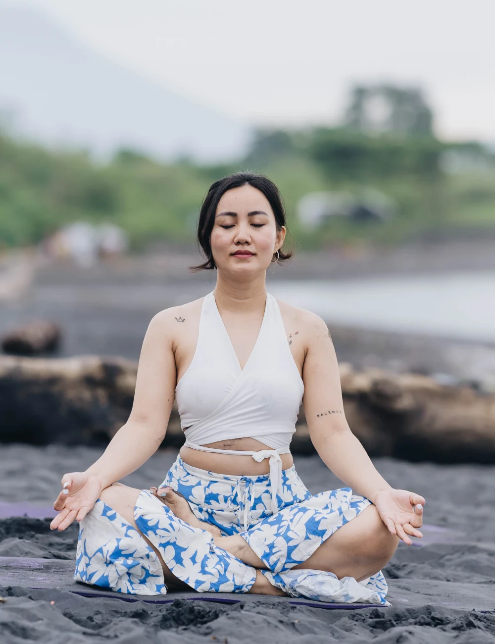 A student meditating cross-legged on a black-sand beach