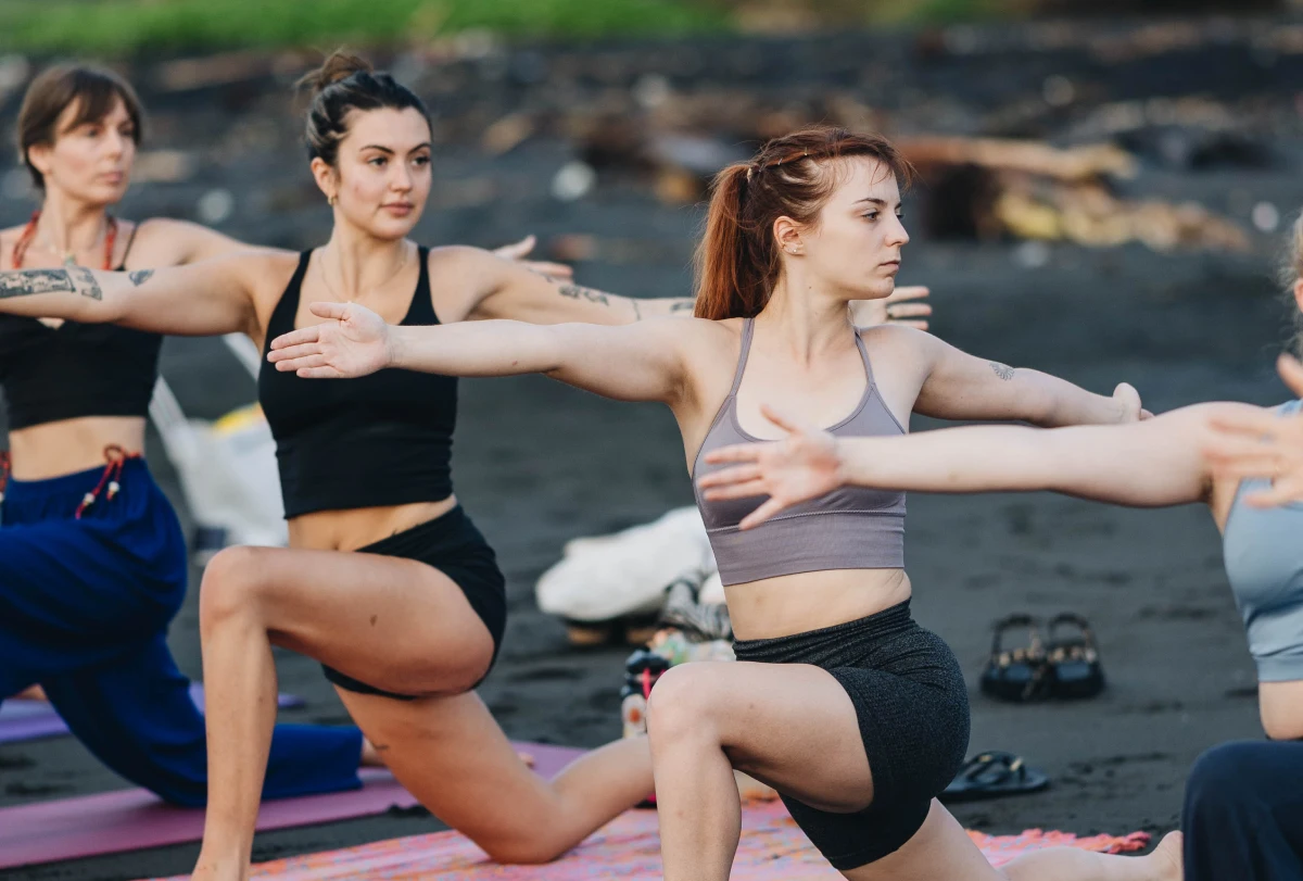 Students in a low lunge with arms extended on a black-sand beach
