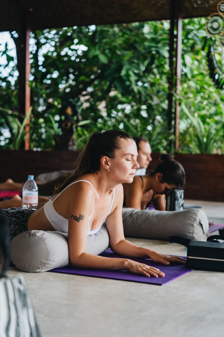 A student resting over a bolster with eyes closed in a jungle shala