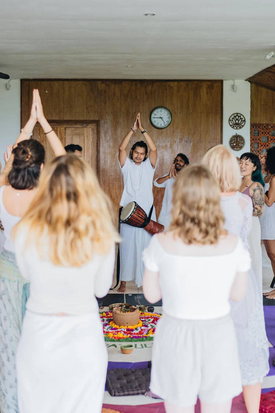 Students in white joining a drum-led ceremony around a flower mandala