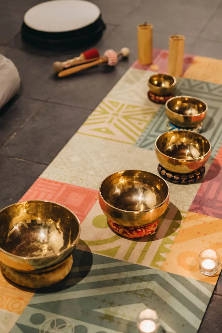 A row of Tibetan singing bowls on a patterned mat beside mallets and candles