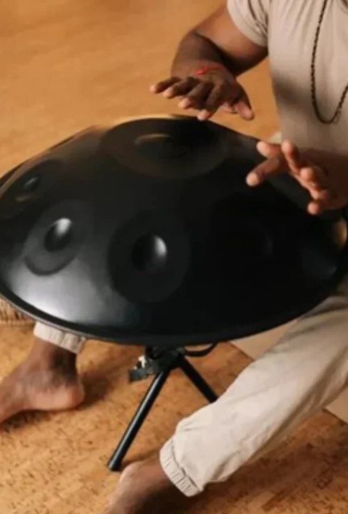 A hand pan on a stand being played on a cork floor