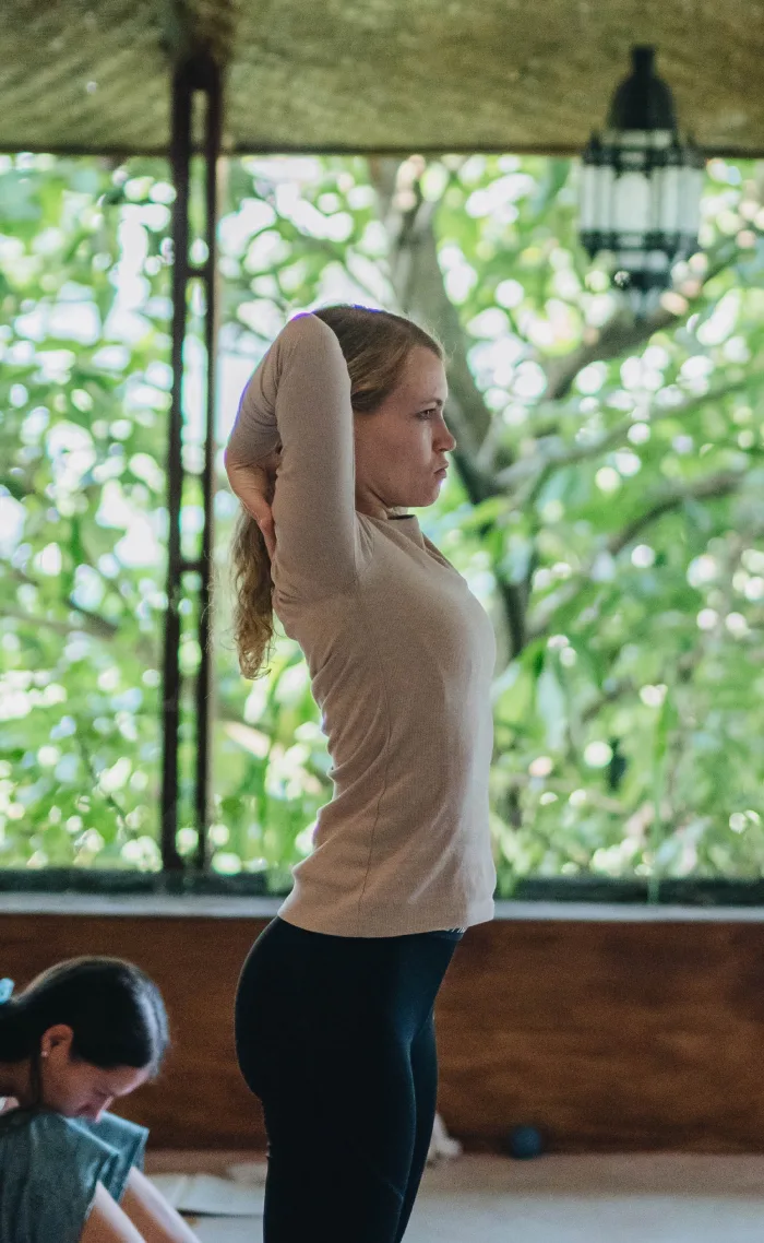 A student in a standing shoulder stretch in an open-air shala
