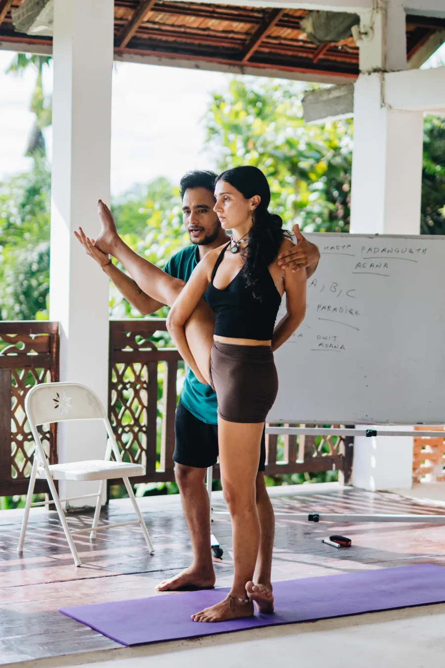 A teacher adjusting a student in a standing leg-raise pose