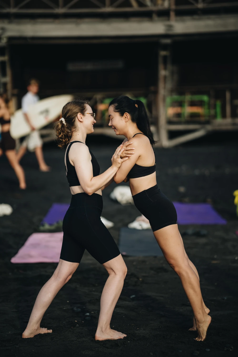 Two students practising a partner stretch on a black-sand beach