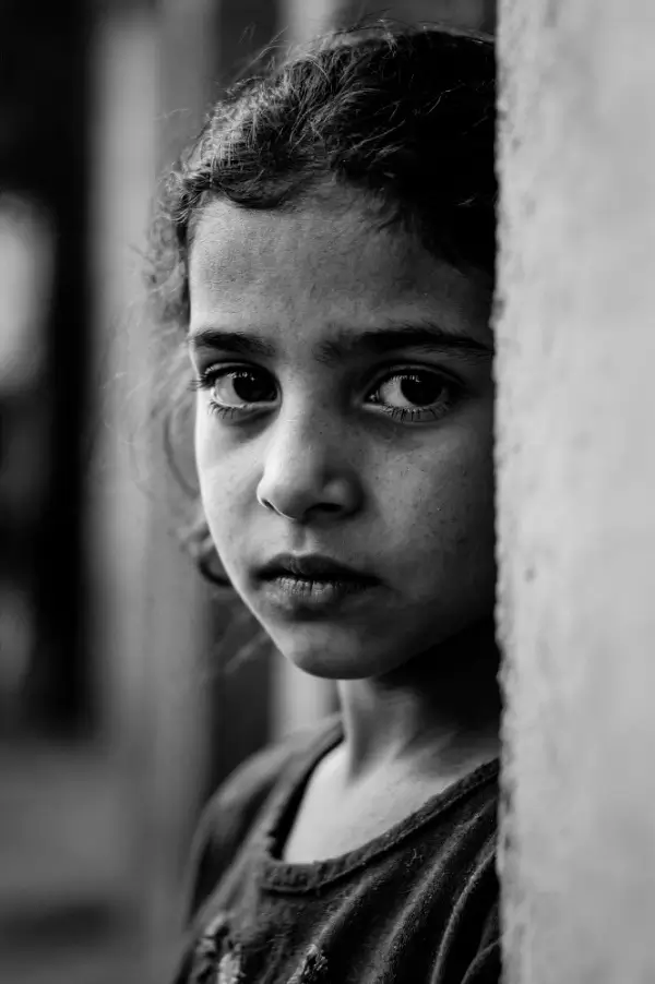 Black and white portrait of a young girl looking out from behind a wall