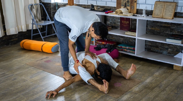 A teacher adjusting a student in a supine twist
