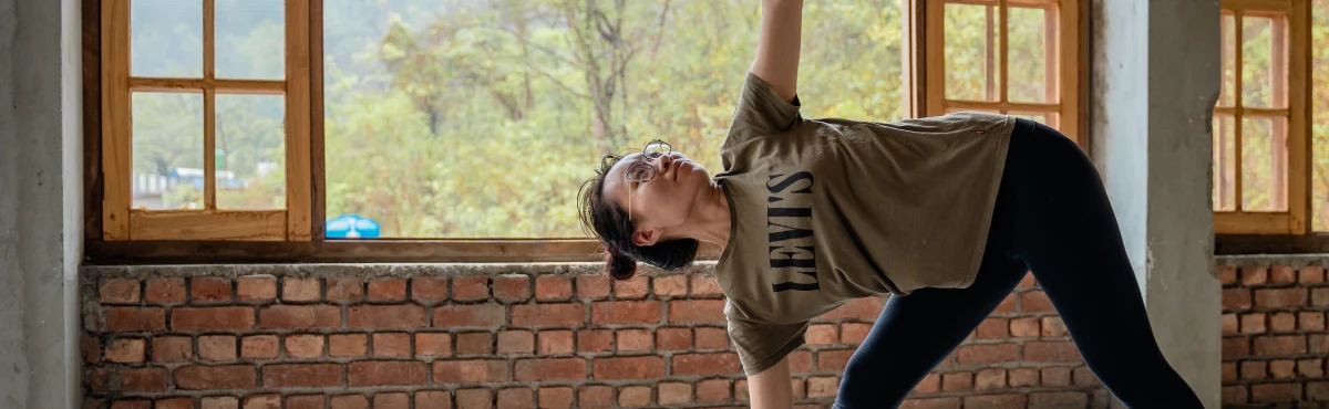 A student in triangle pose by the yoga hall windows