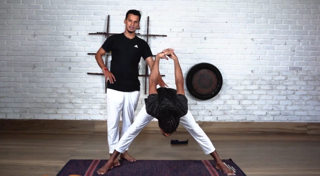 A teacher guiding a student in a wide-leg forward fold