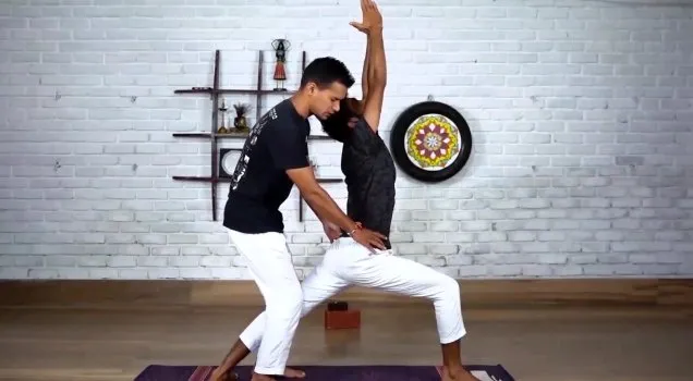 A teacher adjusting a student's hips in Warrior I