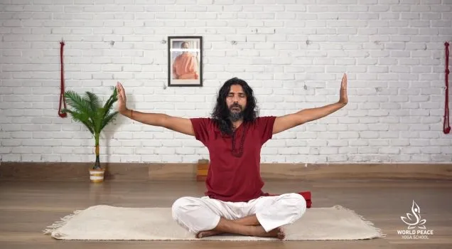A teacher seated cross-legged with arms raised during a guided practice