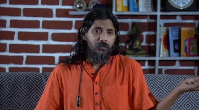 A teacher discussing yoga philosophy in front of a bookshelf
