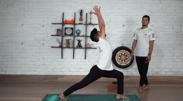 A teacher observing a student in Warrior I with arms raised