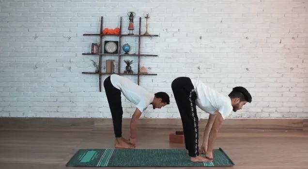 A teacher and student practising a standing forward fold side by side