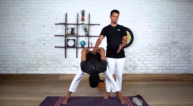 A teacher guiding a student in Prasarita Padottanasana
