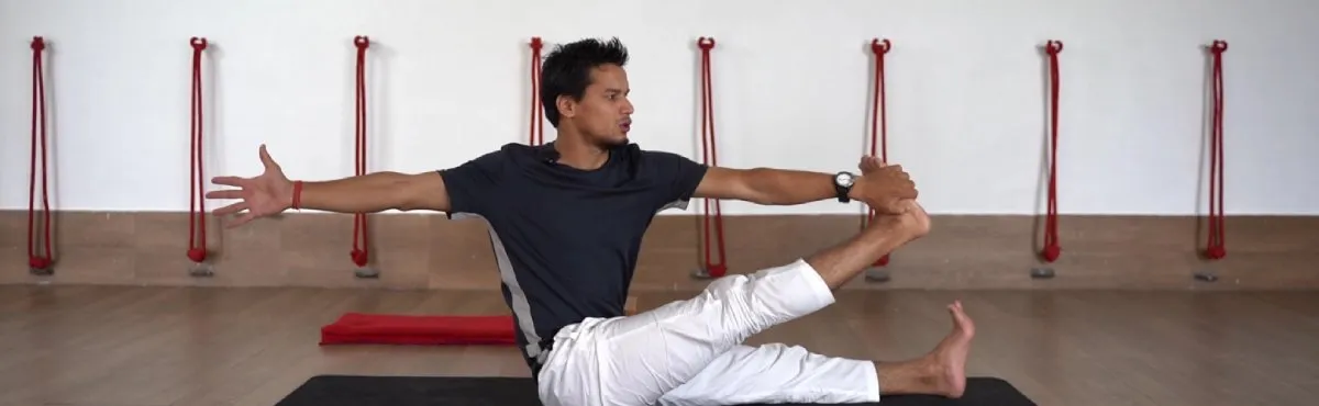 A teacher demonstrating a seated Ashtanga pose with one leg raised