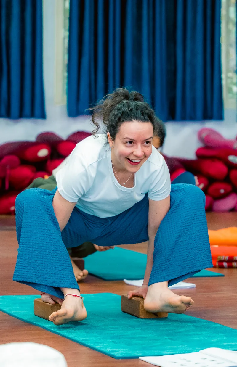 A smiling student in a supported squat on yoga blocks