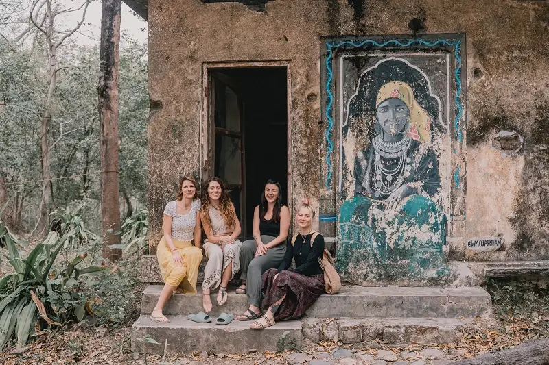 Four students sitting on the steps of a mural-painted hut at the Beatles Ashram