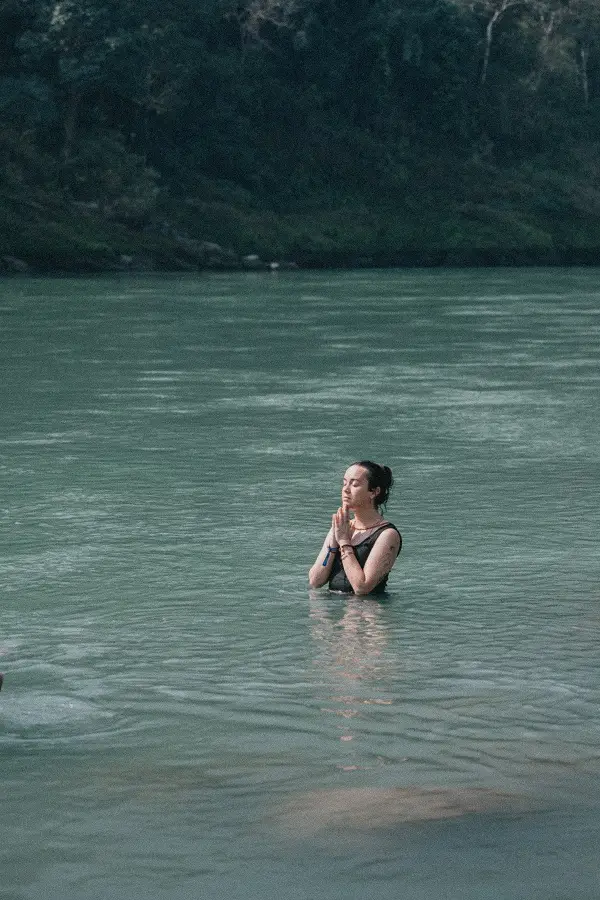 A student standing waist-deep in the Ganga with palms joined