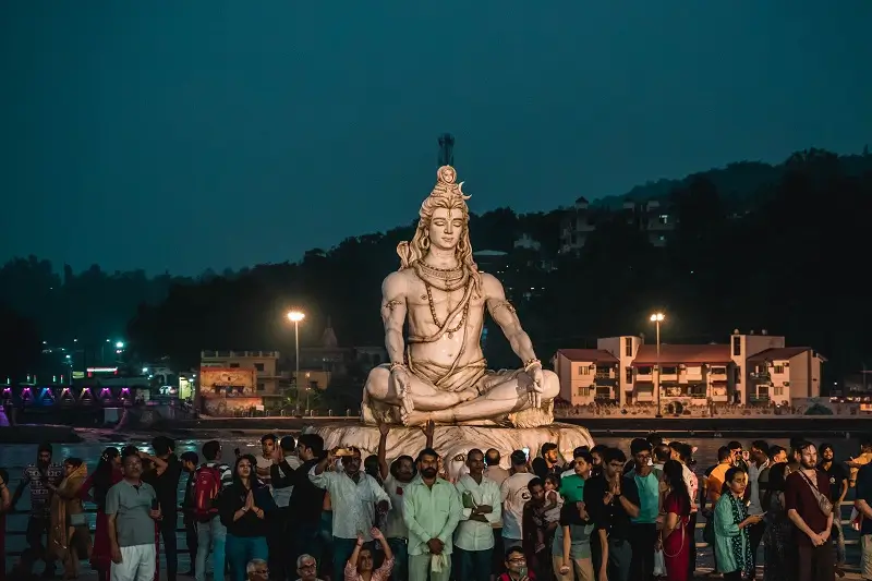 A crowd gathered at dusk around the Shiva statue on the Ganga ghat at Parmarth Niketan