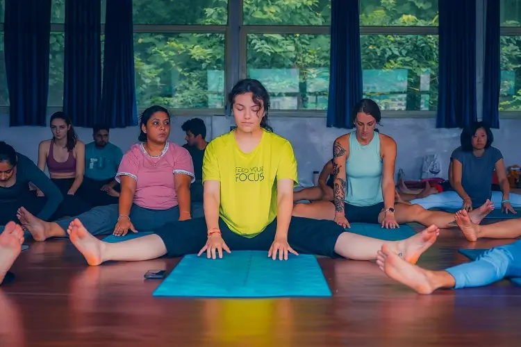 Students seated in a straddle stretch during a Kundalini class