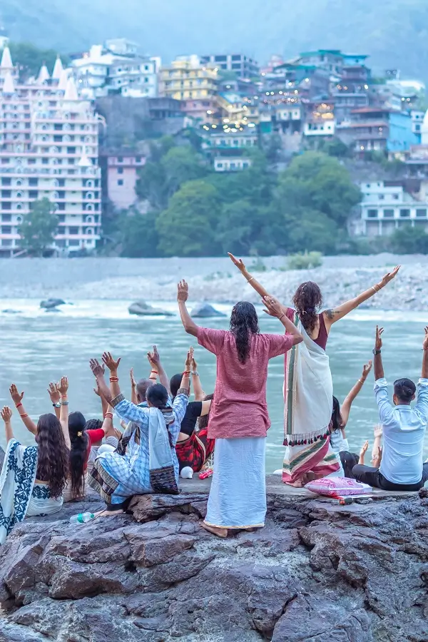 A group practising on the rocks beside the Ganga at Rishikesh, with the town on the far bank
