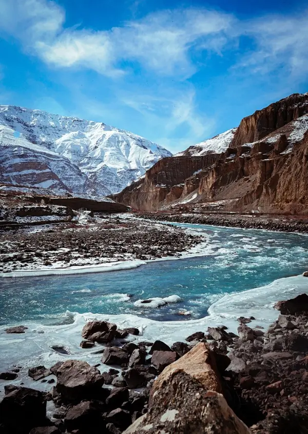 A glacial river flowing past snow-capped Himalayan cliffs