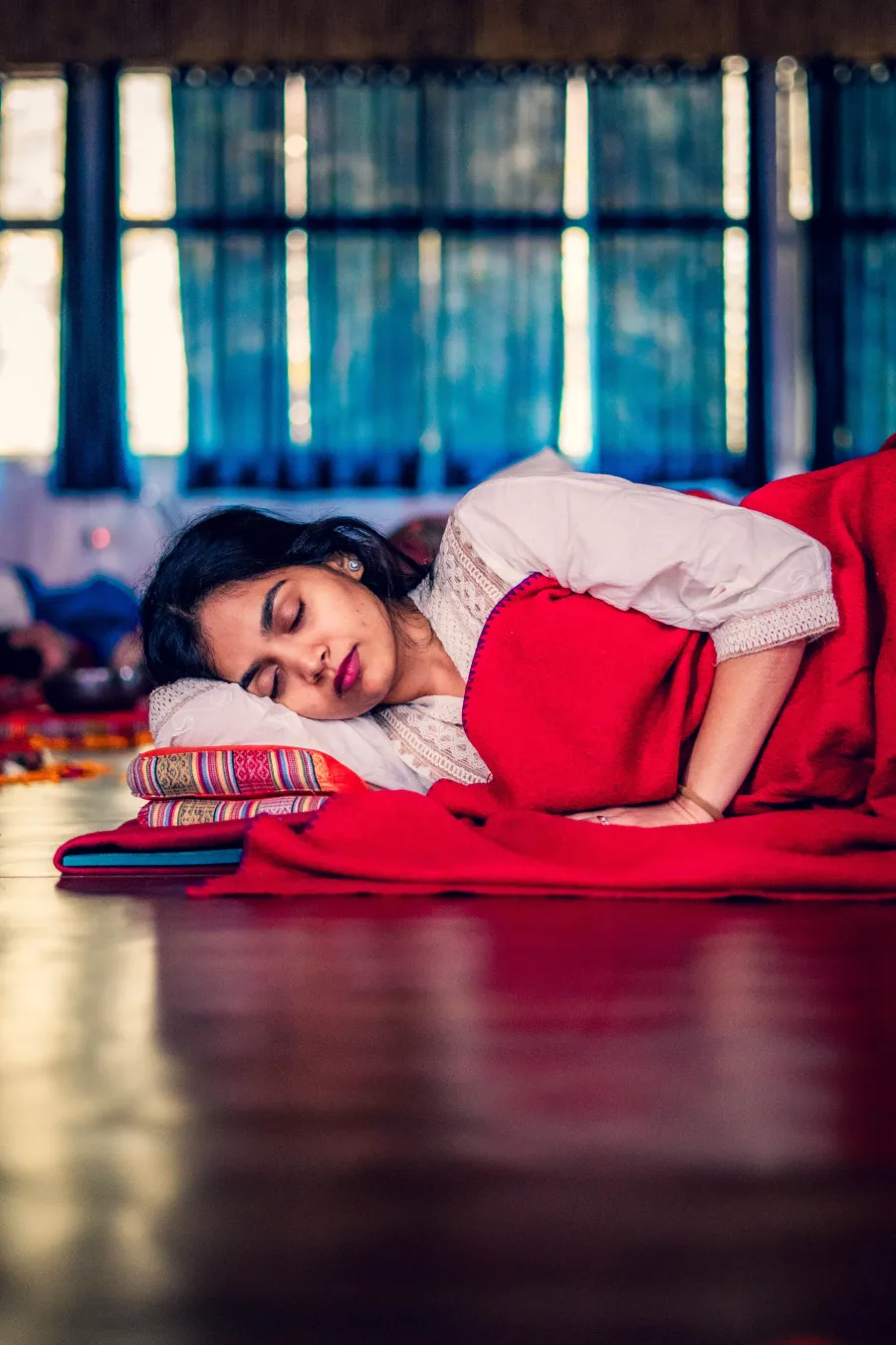 A student resting on her side under a red blanket during Yoga Nidra
