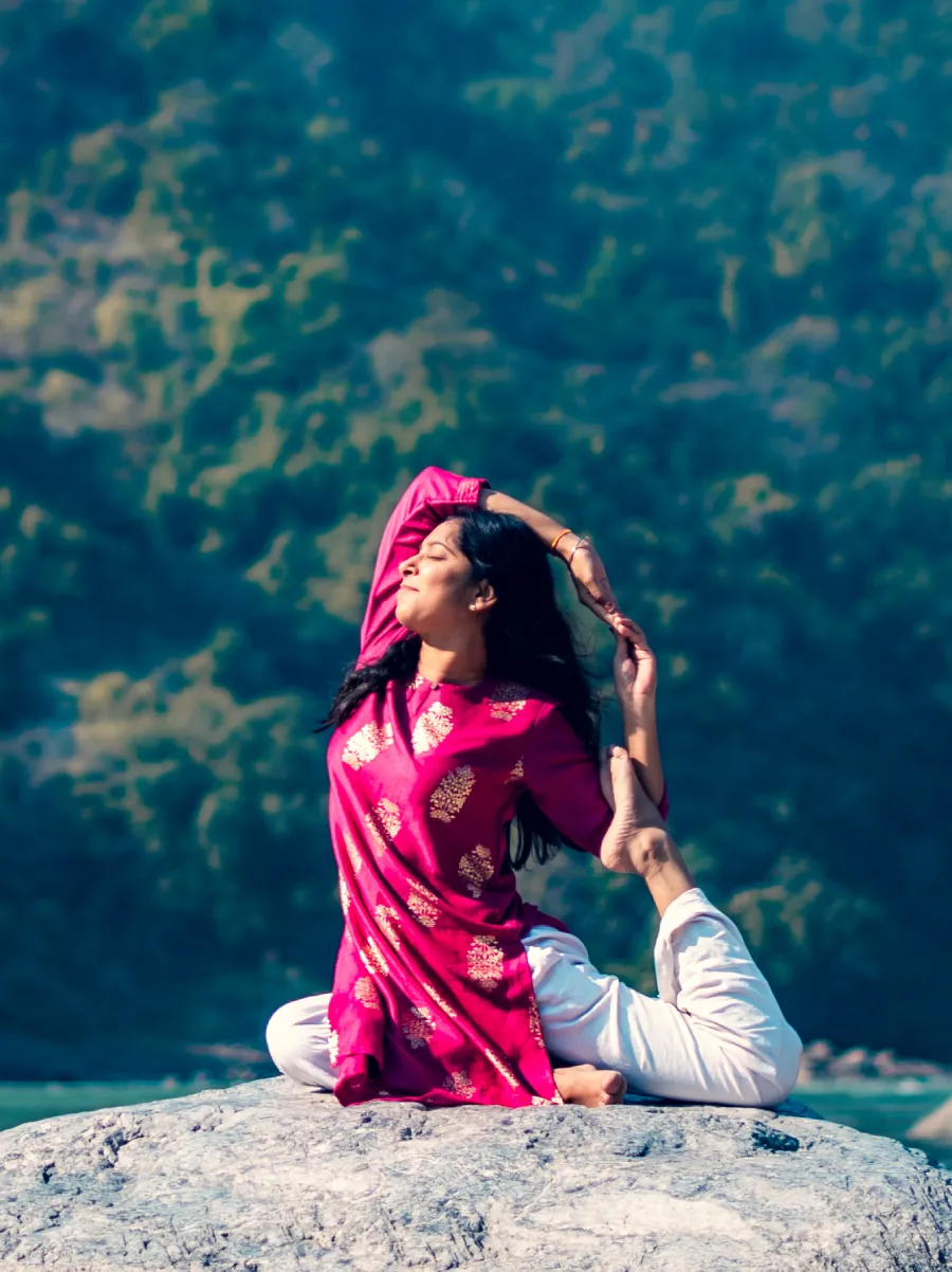 A student in a seated backbend on a rock beside the Ganga