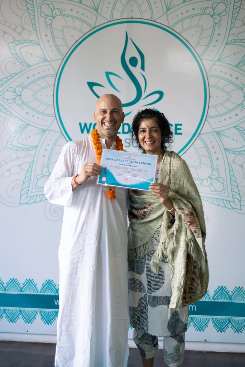 A graduate holding a World Peace Yoga School certificate beside Maa Haripriya