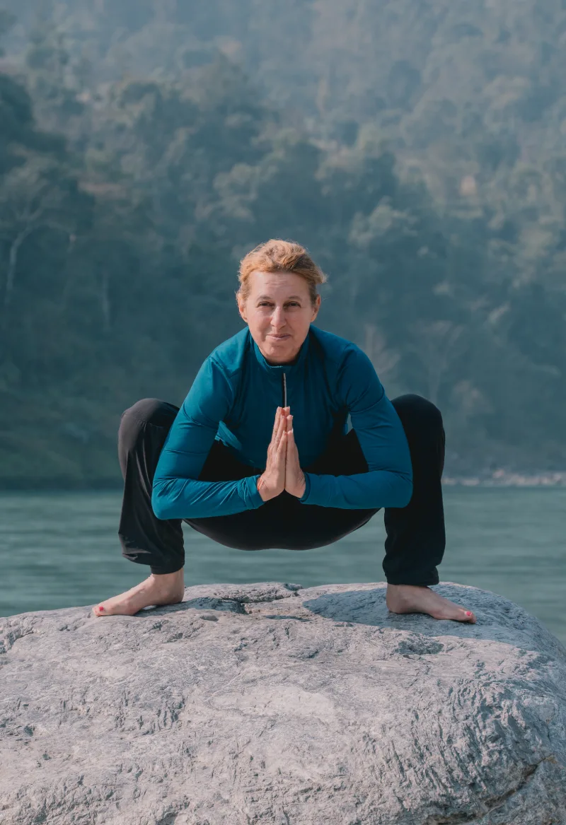 A student in garland pose on a rock by the Ganga