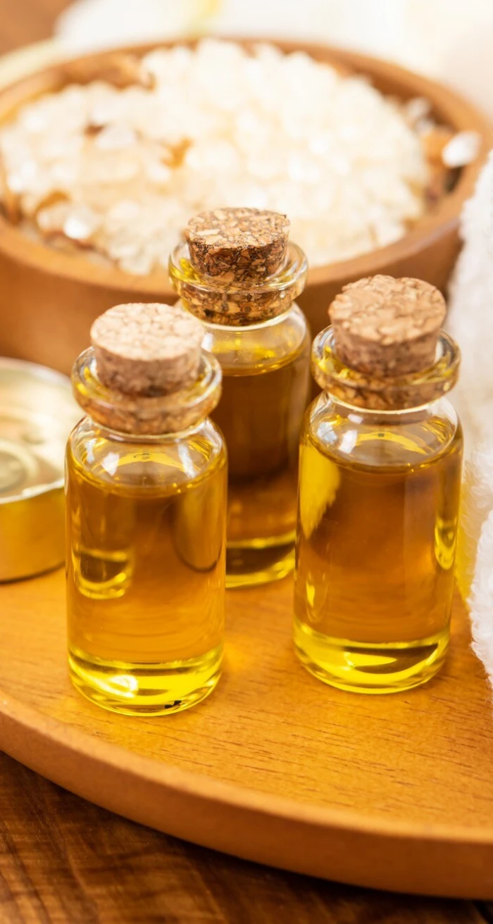 Three corked bottles of herbal massage oil beside a bowl of bath salt