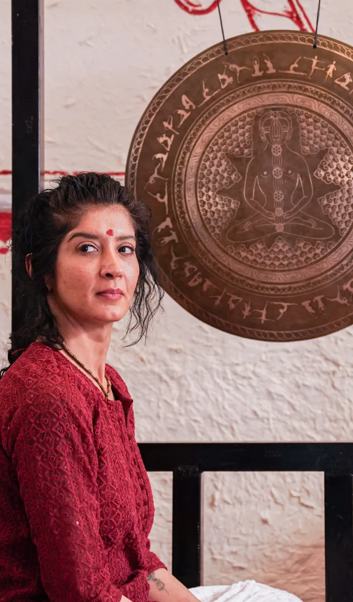 A woman seated beside a large engraved chakra gong