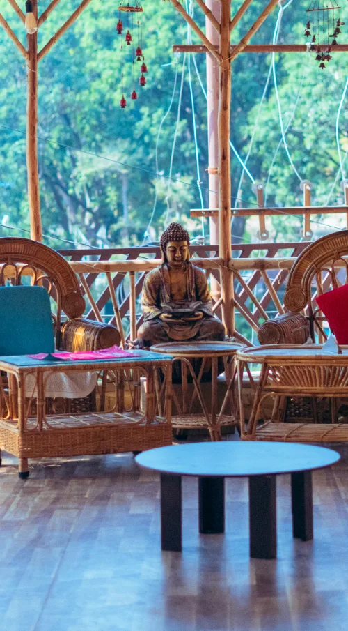 A cane-furnished lounge with a Buddha statue and wind chimes