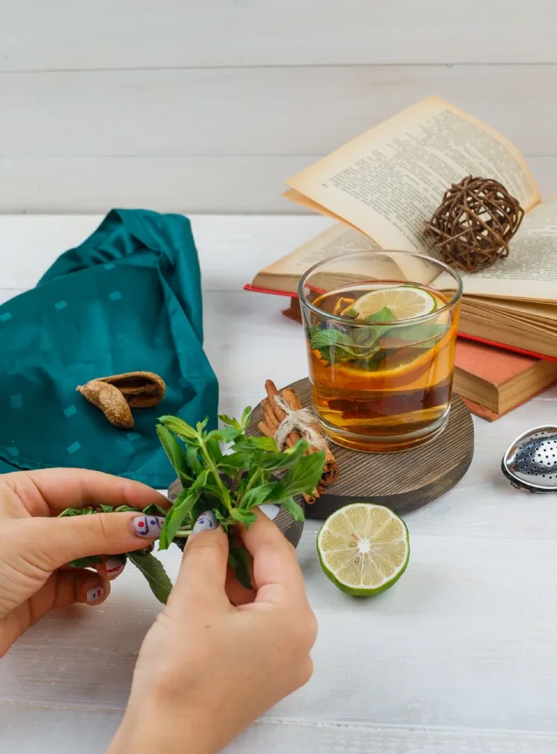 Hands sorting fresh herbs beside a glass of herbal tea