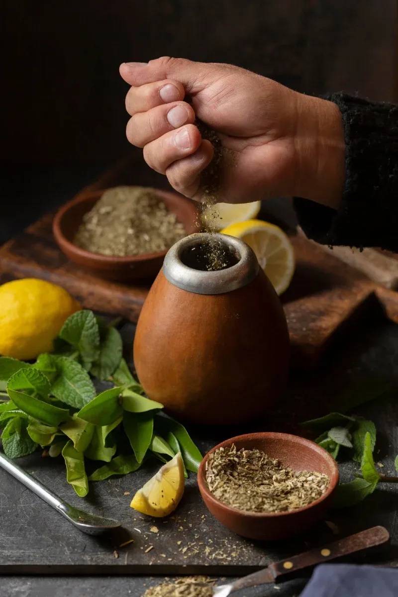 A hand sprinkling herbal powder beside a gourd, lemons, and fresh leaves