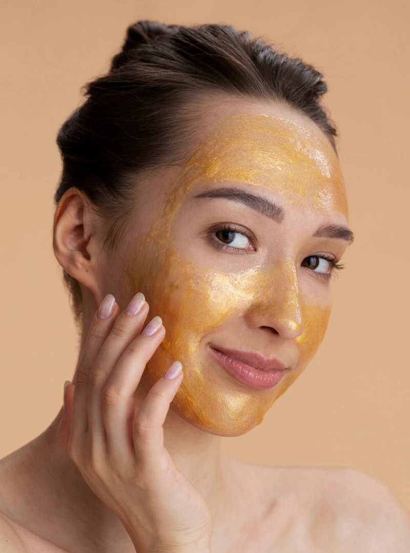 A smiling woman with a golden turmeric mask on her face